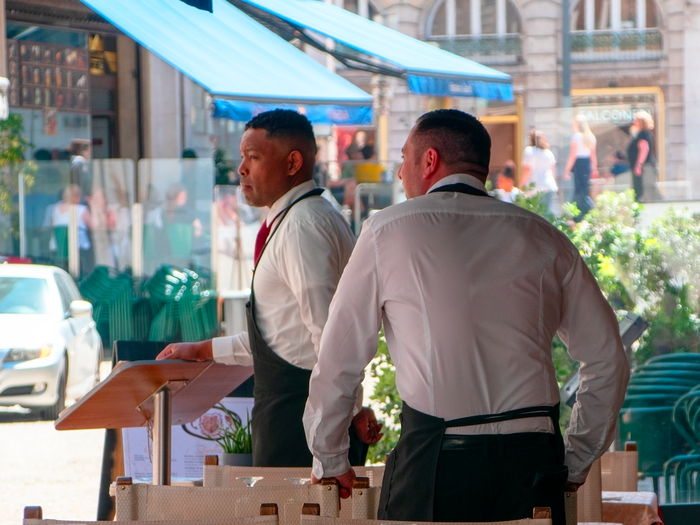 Two waiters in the terrace of a restaurant looking to attract clients
