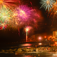 Fireworks going off over the beach with people celebrating around bonfires