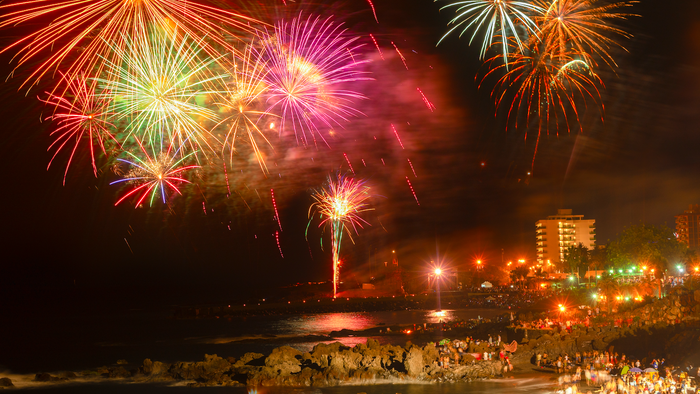 Fireworks going off over the beach with people celebrating around bonfires
