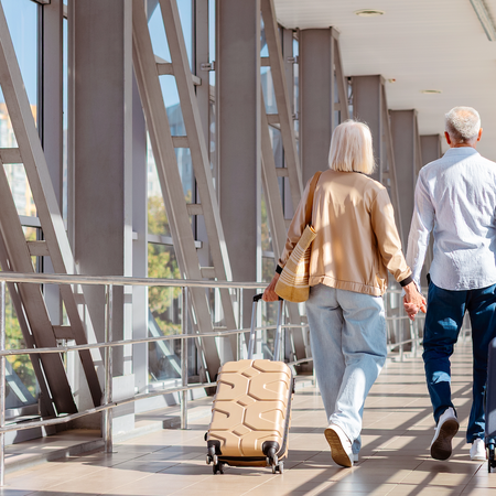 Retired couple walking together dragging their suitcases