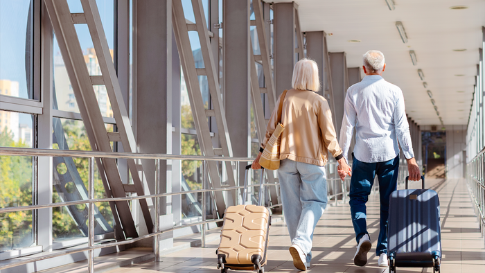 Retired couple walking together dragging their suitcases