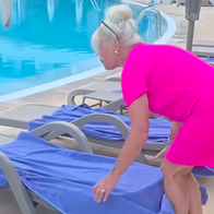 Woman in bright pink dress removes towels from sunbeds by a pool