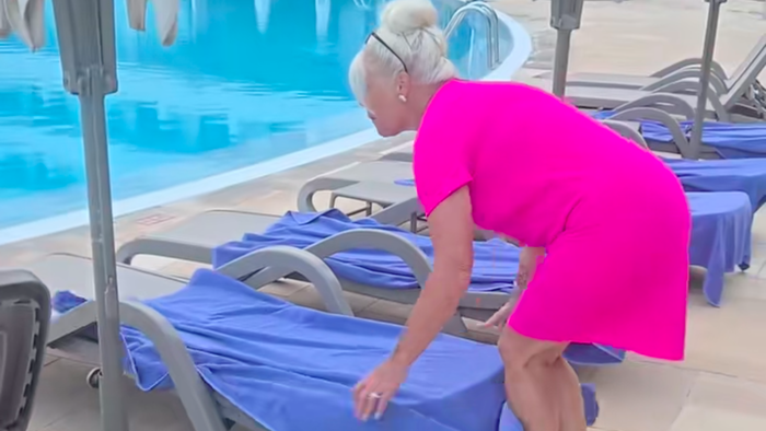 Woman in bright pink dress removes towels from sunbeds by a pool