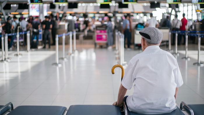 Elder man sitting in front of a check in area of an airport waiting for his family