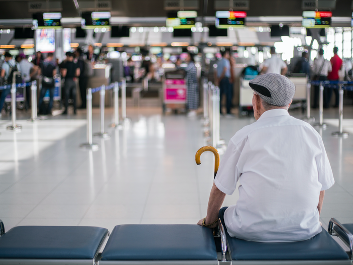 Elder man sitting in front of a check in area of an airport waiting for his family