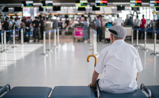 Elder man sitting in front of a check in area of an airport waiting for his family