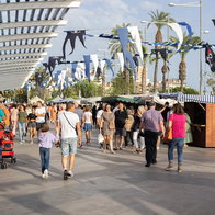Families and visitors stroll through a busy outdoor promenade in Spain during a local festival and public holiday celebration.