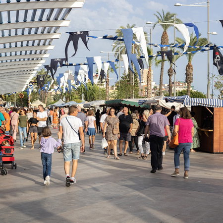 Families and visitors stroll through a busy outdoor promenade in Spain during a local festival and public holiday celebration.