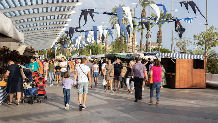 Families and visitors stroll through a busy outdoor promenade in Spain during a local festival and public holiday celebration.