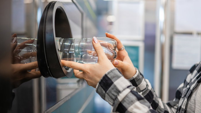Customer inserts an empty plastic bottle into a recycling return machine as part of a deposit return scheme for beverage containers.