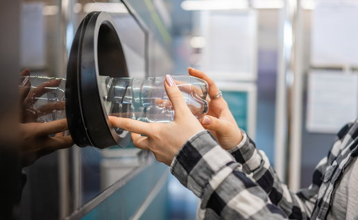 Customer inserts an empty plastic bottle into a recycling return machine as part of a deposit return scheme for beverage containers.