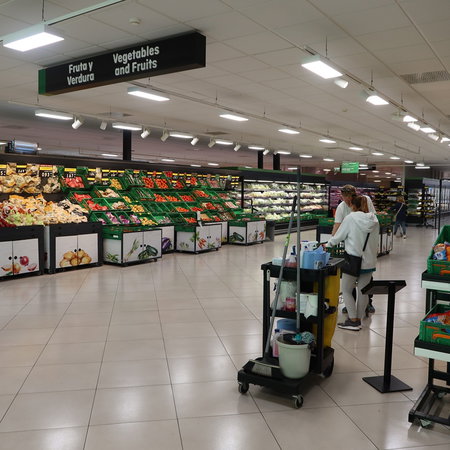 Inside a Spanish supermarket fruit and vegetable section, with fresh produce displays and bilingual signage above the aisles.
