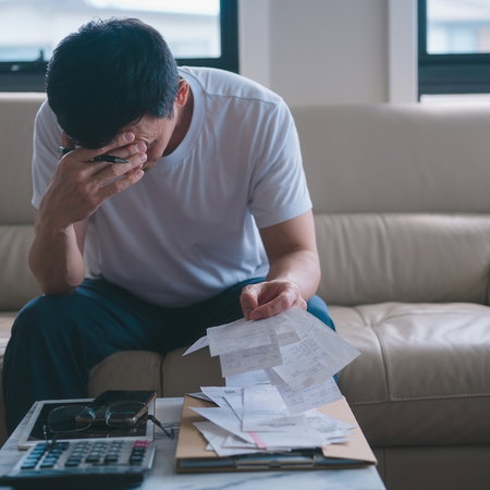 Worried man reviewing bills and financial documents at home amid debt concerns.
