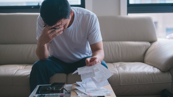 Worried man reviewing bills and financial documents at home amid debt concerns.