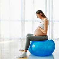 Happy young pregnant woman sitting on a ball doing excerises at home