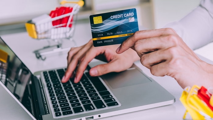 Person making an online purchase with a credit card while shopping on a laptop.