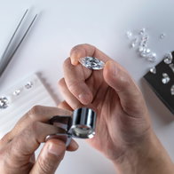 A gem expert examines a loose diamond with a loupe beside other stones on a white table.