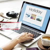 Traveller booking a holiday online using a laptop, with travel tickets and holiday accommodation options displayed on screen.