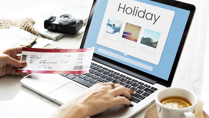 Traveller booking a holiday online using a laptop, with travel tickets and holiday accommodation options displayed on screen.