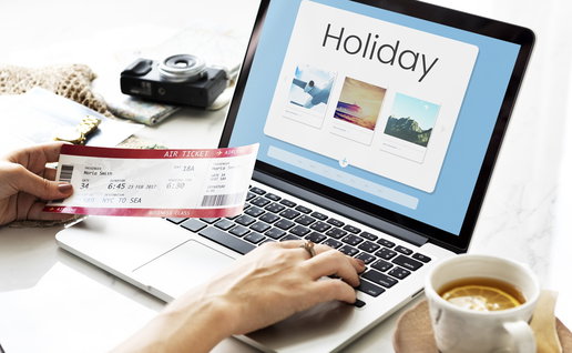Traveller booking a holiday online using a laptop, with travel tickets and holiday accommodation options displayed on screen.