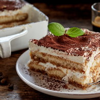 Close up on a portion of gourmet tiramisu Italian dessert topped with a sprig of mint served on a plate at table in a side view