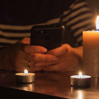A mobile phone in hand with burning candles around due to a blackout