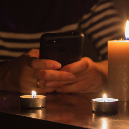 A mobile phone in hand with burning candles around due to a blackout
