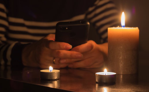 A mobile phone in hand with burning candles around due to a blackout
