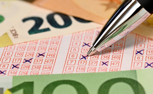 Detailed close-up of a ballpoint pen tip while writing crosses on numbers on a lottery ticket surrounded by euro banknotes