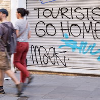 Shop blinds with ''Tourists go home'' written on them as a couple walks past