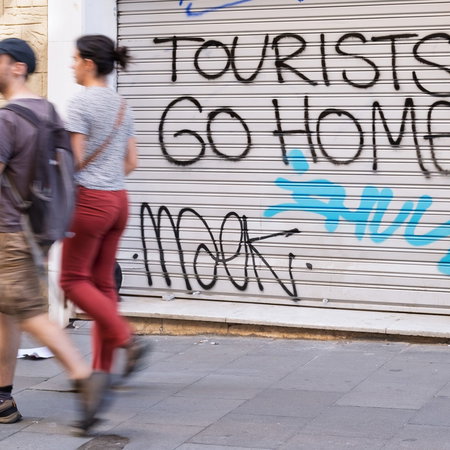 Shop blinds with ''Tourists go home'' written on them as a couple walks past