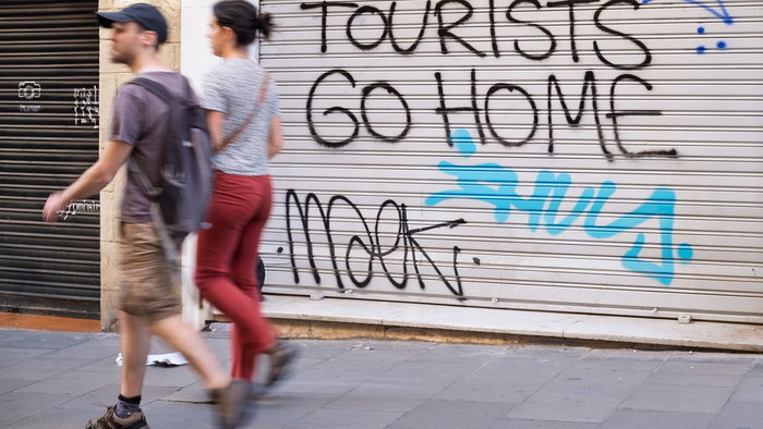 Shop blinds with ''Tourists go home'' written on them as a couple walks past