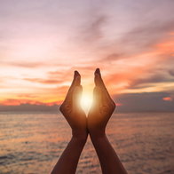 Hands framing the sun during a colourful sunrise over the sea on the day of the summer solstice.