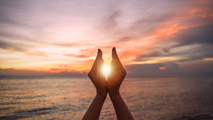 Hands framing the sun during a colourful sunrise over the sea on the day of the summer solstice.
