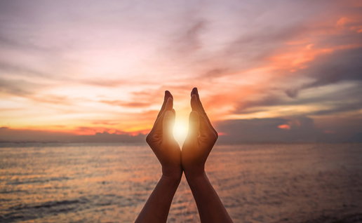 Hands framing the sun during a colourful sunrise over the sea on the day of the summer solstice.