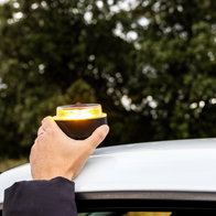 A driver places a connected V16 emergency beacon on the roof of a vehicle during a roadside stop in Spain.