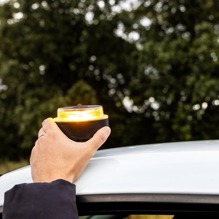 A driver places a connected V16 emergency beacon on the roof of a vehicle during a roadside stop in Spain.