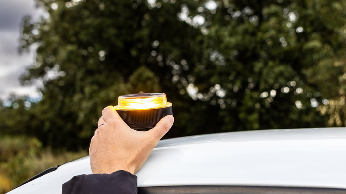 A driver places a connected V16 emergency beacon on the roof of a vehicle during a roadside stop in Spain.