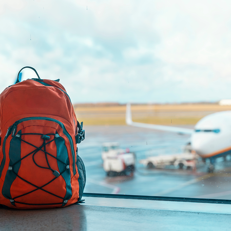 Red backpack beside an airport terminal window with passenger planes parked outside.