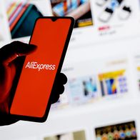 erson holding a smartphone displaying the AliExpress logo in front of an online shopping page.