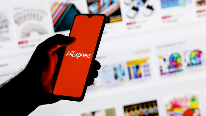 erson holding a smartphone displaying the AliExpress logo in front of an online shopping page.
