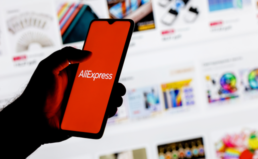 erson holding a smartphone displaying the AliExpress logo in front of an online shopping page.