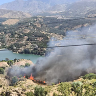 Flames and thick black smoke rising from hillside vegetation beside the Béznar reservoir.