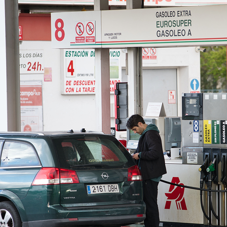 Driver filling a car at a petrol station beside a Spanish motorway during a summer journey.