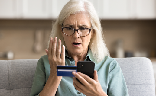 Older woman holding a bank card and looking worried at her phone.