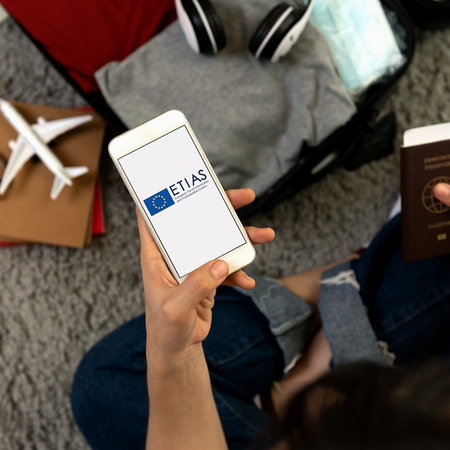 Traveller holding a passport and smartphone displaying the ETIAS logo while preparing for a trip to Europe.