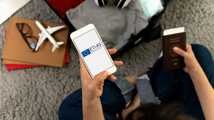 Traveller holding a passport and smartphone displaying the ETIAS logo while preparing for a trip to Europe.