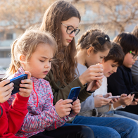 Children sitting together on a wall and looking at a smartphone.