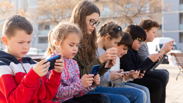 Children sitting together on a wall and looking at a smartphone.