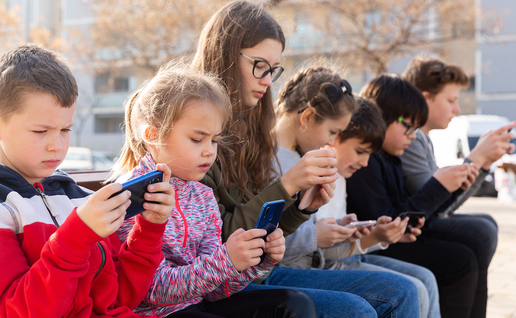Children sitting together on a wall and looking at a smartphone.